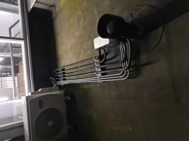 Buitenunit met leidingwerk tegen een donkere wand