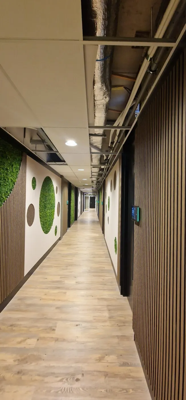 Lange kantoorgang met mosschilderijen en houten lamellen